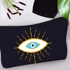 May include: Black zippered makeup bag with a white evil eye design with a blue iris and gold accents.