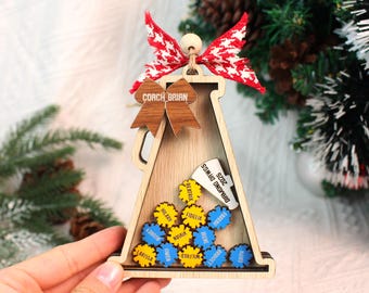 May include: Wooden megaphone-shaped ornament with a red and white patterned bow and wooden accents. The ornament has the text "COACH BRIAN" and "DIAMOND DAWGS 2025". It also features several small, colorful name tags.