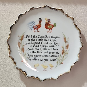 May include: A decorative white plate with a scalloped gold rim. The plate features illustrations of two roosters and three chicks, with text from a children's rhyme. The plate is a charming piece of kitchen decor.