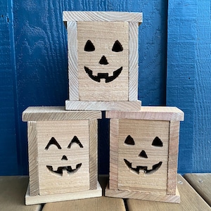 May include: Three wooden jack-o'-lantern candle holders with carved faces. The candle holders are stacked on top of each other, with the top one being the largest.