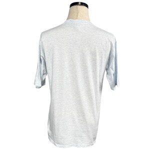 May include: A light gray short-sleeve t-shirt. The shirt is displayed on a mannequin. The fabric has a heathered appearance. The sleeves are short and the neckline is crew-cut. The shirt is a basic, casual style.