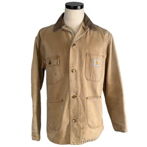 Può includere: Giacca Carhartt color cachi con colletto in velluto a coste marrone. La giacca ha quattro tasche frontali, una chiusura con bottoni e il logo Carhartt sulla tasca frontale. La giacca è esposta su un manichino.