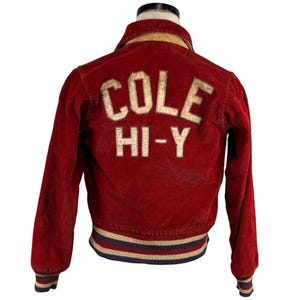 Puede incluir: Chaqueta de pana roja con el texto "COLE HI-Y" en letras color crema en la espalda. La chaqueta tiene cuello y puños acanalados con rayas azules, blancas y rojas. La chaqueta se exhibe en un maniquí.