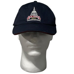 Op de afbeelding: Een donkerblauwe baseballpet met een rode rand. De voorkant van de pet heeft een geborduurd logo voor de US Open 2011 in Congressional.