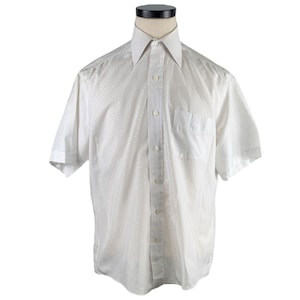 Puede incluir: Camisa blanca de manga corta con un sutil estampado de puntos. La camisa tiene un cuello clásico, una botonadura frontal y un bolsillo en el pecho. La camisa se muestra en un maniquí.