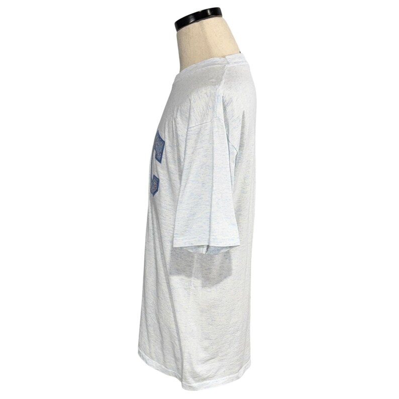 May include: A light gray t-shirt with a blue design on the front. The short-sleeved shirt is displayed on a mannequin. The fabric appears to be a soft, lightweight material.
