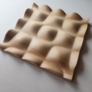 May include: A wooden wall panel with a textured surface. The panel has a grid pattern with raised squares and a wavy edge.