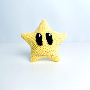 Puede incluir: Una estrella amarilla hecha a mano con ojos negros y reflejos blancos. La estrella tiene cinco puntas y una superficie texturizada. El juguete es probablemente un personaje de videojuego.