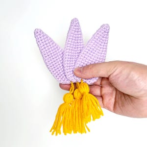 May include: A handmade crochet crown in a soft lavender color, featuring three pointed petals. The crown is adorned with bright yellow tassels, adding a playful contrast. This whimsical accessory is perfect for themed parties or imaginative play.