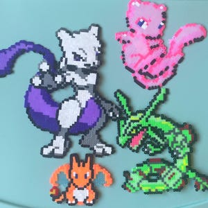 May include: Five different Pokemon characters made with perler beads. The characters are Mewtwo, Charizard, Venusaur, Gengar, and Jigglypuff. The beads are arranged in a pixelated style to create the characters.