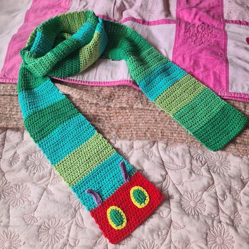May include: A green, blue, and red crocheted scarf with a caterpillar design. The caterpillar has a red body with green and yellow eyes.