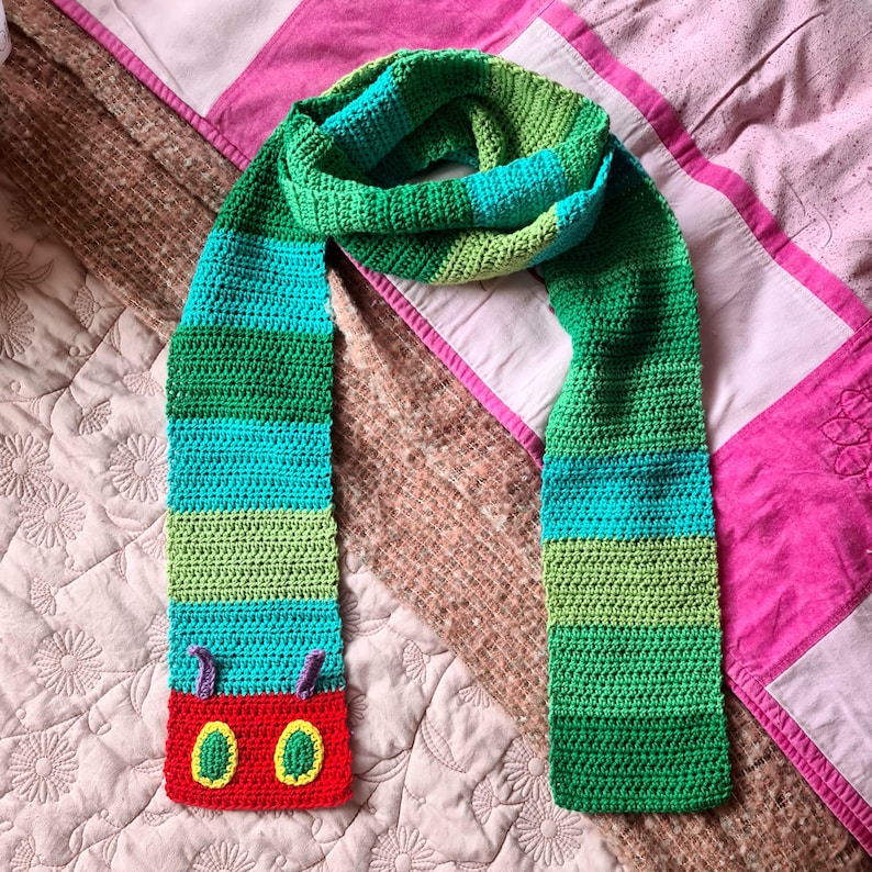 May include: A green, blue, and red striped crocheted scarf with a colorful caterpillar face on the end.