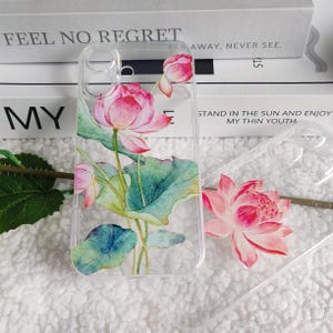 May include: A clear phone case with a watercolor design of pink lotus flowers and green leaves. The case has a raised edge around the camera lens.