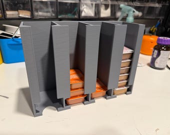 Peut inclure: Un organisateur de rangement gris imprimé en 3D en plastique doté de quatre fentes verticales conçues pour contenir de petits récipients alimentaires rectangulaires. L'unité possède une base solide avec des découpes pour accéder aux articles.