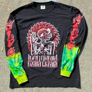 以下が含まれることがあります： 赤と白のスケルトンデザインのグラフィックが特徴の黒い長袖Tシャツ。袖は赤、緑、黄色のタイダイ効果があります。「King Gizzard and the Lizard Wizard」の文字が前面にプリントされています。