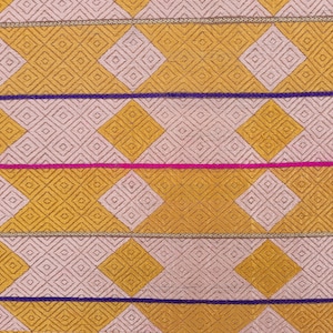 May include: A close-up of a fabric with a repeating pattern of pink and yellow diamonds. The fabric has three horizontal stripes of gold, purple, and pink thread.
