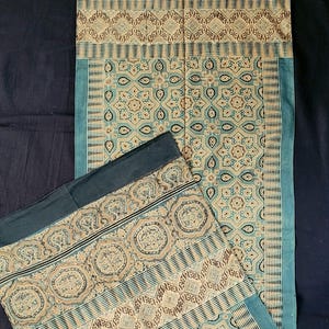 May include: A rectangular textile runner featuring a repeating geometric pattern in shades of teal, beige, and black. The design includes intricate star-shaped motifs, diamond shapes, and decorative borders with circular patterns along the edges.