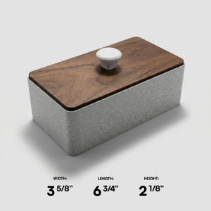 May include: A rectangular box with a wooden lid and a white knob. The box is 3 5/8 inches wide, 6 3/4 inches long, and 2 1/8 inches high. The base is a speckled gray, and the lid is a dark brown wood.