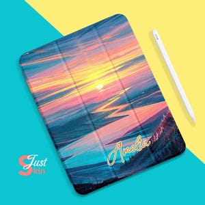 Könnte beinhalten: Eine iPad-Hülle mit einem farbenfrohen Sonnenuntergangslandschaft-Design und dem Namen "Amelia" in goldenen Buchstaben.