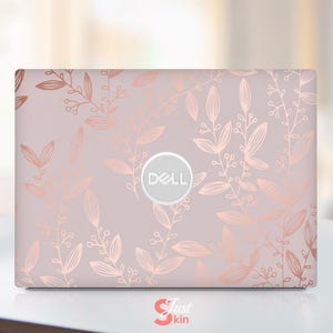 Könnte beinhalten: Eine Dell Laptop-Hülle mit hellrosa Hintergrund und einem roségoldenen Blumendesign aus Blättern und Zweigen. Das Dell-Logo befindet sich in der Mitte. Der Text "Just Skin" befindet sich unten links.