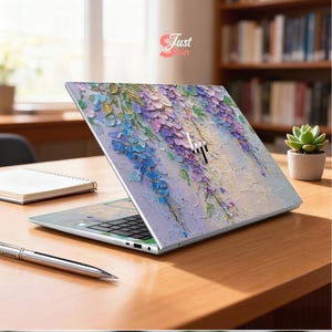 K&ouml;nnte beinhalten: Ein ge&ouml;ffnetes HP-Laptop mit einem Blumendesign in Blau-, Lila- und Wei&szlig;t&ouml;nen. Der Laptop steht auf einem Holztisch, mit einem Stift und einem Notizbuch. Der Text "Just Skin" ist sichtbar.