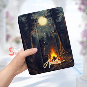 May include: A black and white wolf illustration on a black case with a forest scene and a full moon. The case has the name "Amelia" written in gold lettering.