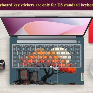May include: Laptop with a custom keyboard skin featuring an industrial scene with a tree and orange leaves. The keyboard keys have a colorful, distressed design. The laptop is open, displaying a pink and white screen. Text at the top reads: "Keyboard key stickers are only for US standard keyboards."