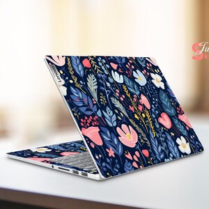 Op de afbeelding: Een Lenovo laptop met een bloemen skin. De skin heeft een donkerblauwe achtergrond met een patroon van roze, witte en gele bloemen, samen met blauwe en groene bladeren. De laptop is open op een wit oppervlak.