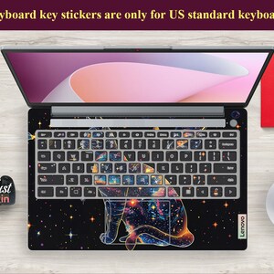 May include: A laptop keyboard with a galaxy and cat design. The keyboard keys are covered with stickers that feature a galaxy design with a cat silhouette. The laptop is a Lenovo.