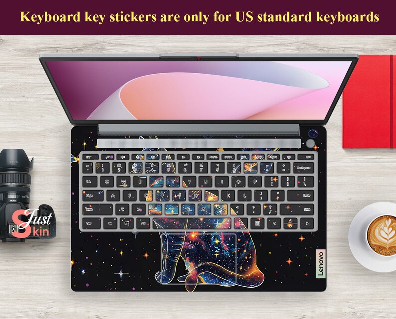 May include: A laptop keyboard with a galaxy and cat design. The keyboard keys are covered with stickers that feature a galaxy design with a cat silhouette. The laptop is a Lenovo.