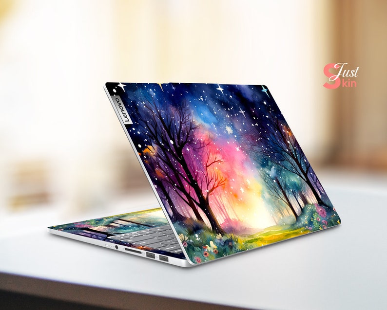 May include: A laptop computer with a colorful watercolor design on the lid. The design features a forest scene with trees, a path, and a starry sky. The laptop is open and the keyboard is visible. The laptop brand is Lenovo.