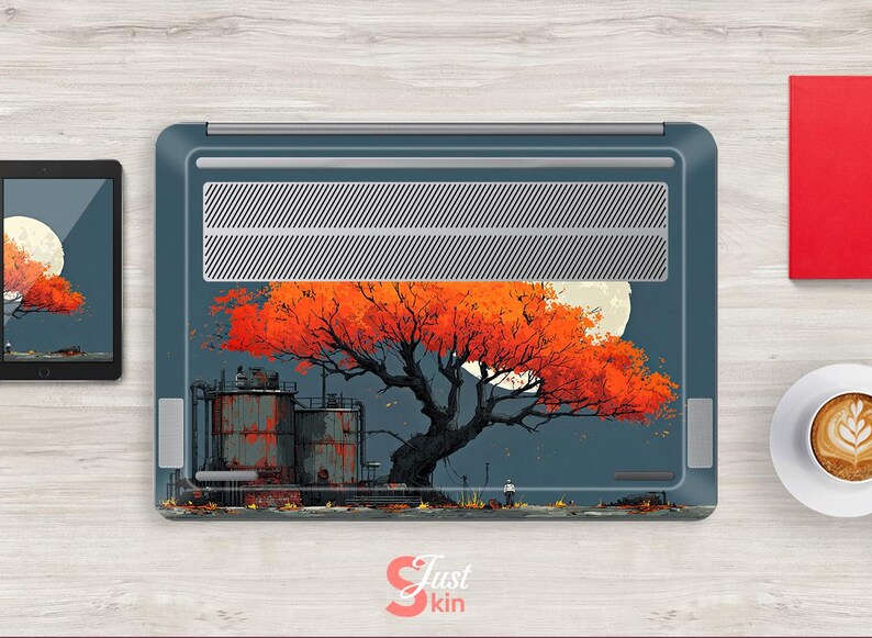 May include: Laptop skin featuring an artistic illustration of a tree with vibrant orange leaves against a full moon. The design includes industrial structures and a figure, set against a dark blue backdrop. The skin is on a laptop, with a tablet and coffee cup nearby.
