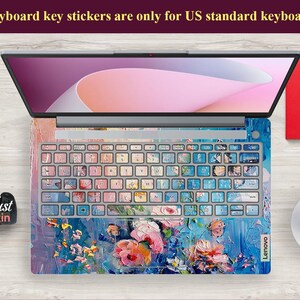 Puede incluir: Un ordenador port&aacute;til con una pegatina de teclado floral de colores. La pegatina presenta un dise&ntilde;o floral azul, rosa y verde con un efecto de pinceladas. El port&aacute;til es de la marca Lenovo.
