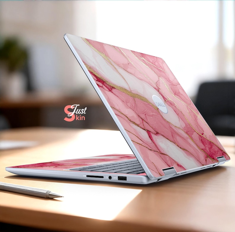 Op de afbeelding: Een laptop met een roze marmerontwerp en gouden accenten. De laptop staat open op een houten oppervlak. De tekst "Just kin" is zichtbaar aan de zijkant.