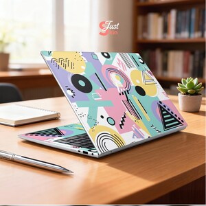May include: Laptop with a colorful geometric design in pastel shades of pink, yellow, teal, and purple. The design includes circles, triangles, and lines. The laptop is open on a wooden desk with a pen and notebook.