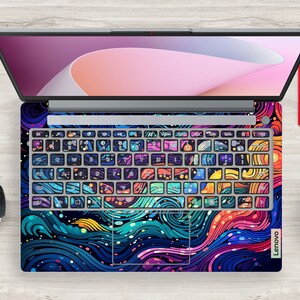 Puede incluir: Un port&aacute;til Lenovo con una llamativa y colorida funda con un dise&ntilde;o abstracto de olas arremolinadas y formas geom&eacute;tricas. Las teclas del teclado est&aacute;n decoradas individualmente con patrones &uacute;nicos. El port&aacute;til est&aacute; abierto.