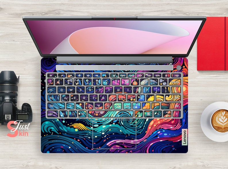 Puede incluir: Un port&aacute;til Lenovo con una llamativa y colorida funda con un dise&ntilde;o abstracto de olas arremolinadas y formas geom&eacute;tricas. Las teclas del teclado est&aacute;n decoradas individualmente con patrones &uacute;nicos. El port&aacute;til est&aacute; abierto.