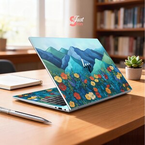 Pode incluir: Um laptop com um design floral e montanhoso colorido. O design apresenta montanhas azuis, flores vermelhas, amarelas e laranjas e folhagem verde. O laptop est&aacute; aberto em uma mesa de madeira.