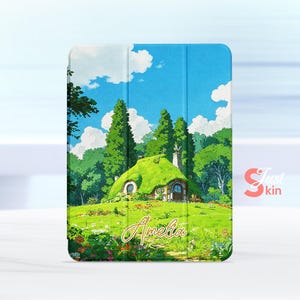 Puede incluir: Una funda para tableta con una ilustración caprichosa de una cabaña con techo verde ubicada en un exuberante paisaje verde bajo un cielo azul brillante con nubes esponjosas. El nombre "Amelia" está escrito en cursiva.