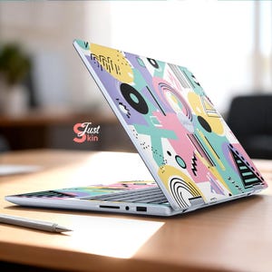May include: A laptop with a colorful abstract design featuring geometric shapes in pastel colors. The design includes circles, lines, and triangles in shades of pink, yellow, blue, and purple. The laptop is open on a wooden surface.