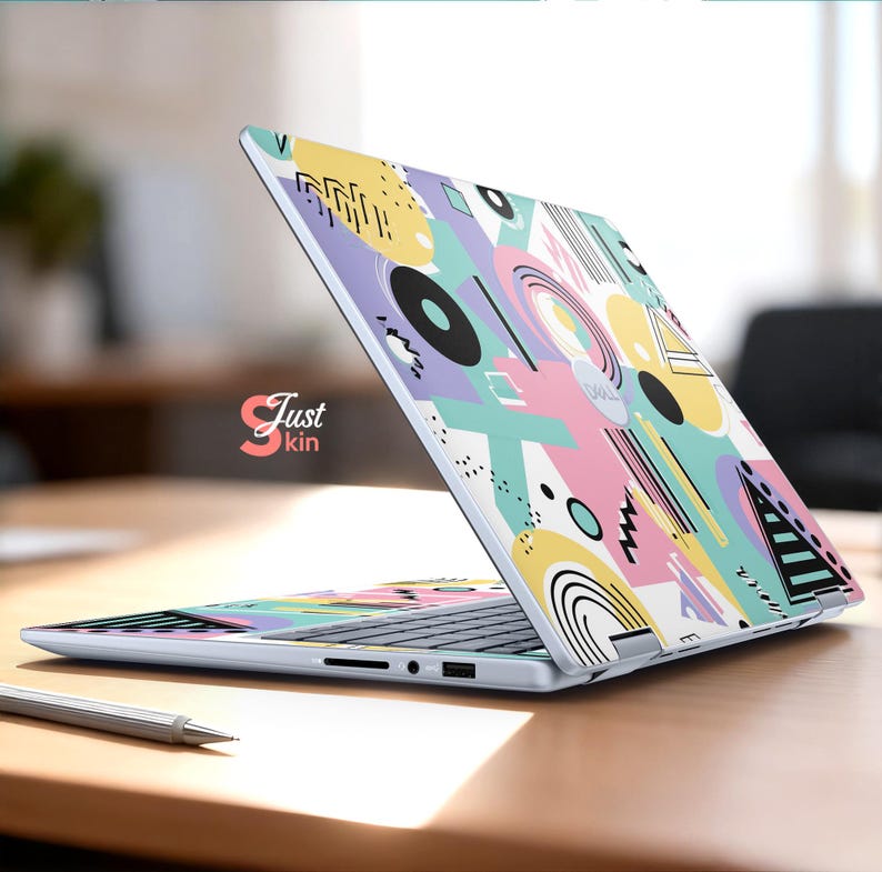 May include: A laptop with a colorful abstract design featuring geometric shapes in pastel colors. The design includes circles, lines, and triangles in shades of pink, yellow, blue, and purple. The laptop is open on a wooden surface.