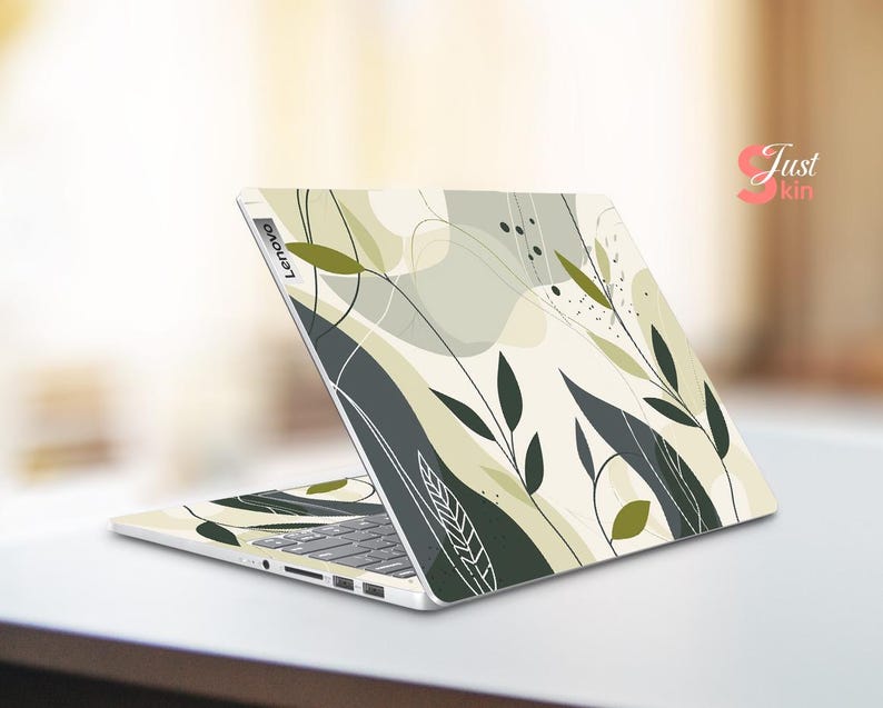 May include: A white laptop with a green and gray abstract floral design on the lid. The design features leaves and swirls. The laptop has the word "Lenovo" printed on the lid.