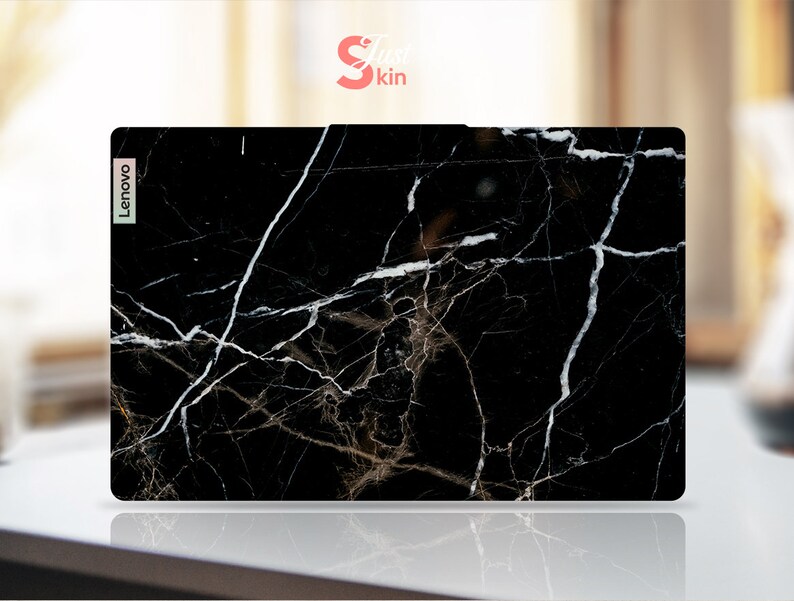 Puede incluir: Piel negra para port&aacute;til con un patr&oacute;n de m&aacute;rmol blanco. La piel tiene la palabra "Lenovo" impresa en el lado izquierdo.