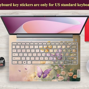 Puede incluir: Un teclado de port&aacute;til con una pegatina de teclado con dise&ntilde;o floral y de mariposa. La pegatina es rosa, amarilla y verde con una mariposa morada en el centro. El texto "Lenovo" es visible en el port&aacute;til.
