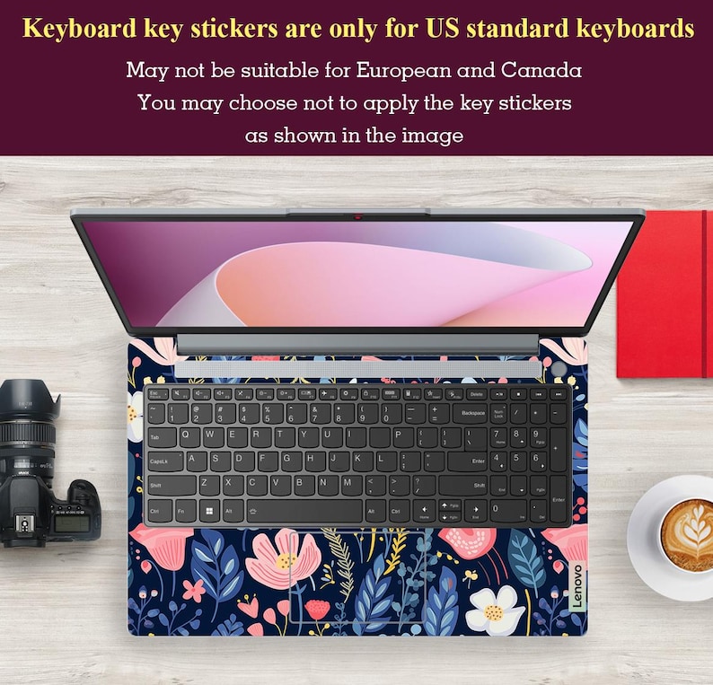 Op de afbeelding: Laptop met een bloemen toetsenbord skin met roze en witte bloemen, blauwe bladeren en een marineblauwe achtergrond. Het laptopscherm toont een roze en witte gradi&euml;nt. Een camera en een kopje koffie zijn zichtbaar.