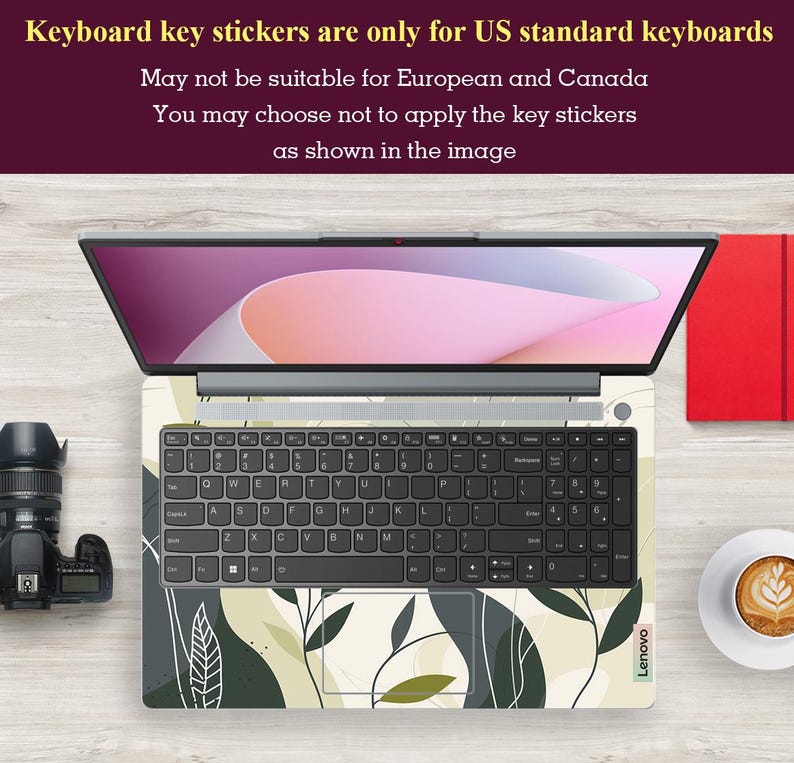 May include: A laptop computer with a keyboard covered in green and white floral key stickers. The laptop is on a wooden surface with a camera and a cup of coffee.