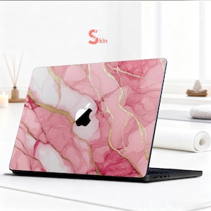 Op de afbeelding: Een laptop met een roze marmer design skin. De skin heeft een patroon van roze en witte wervelingen met gouden aderen. Het Apple-logo is zichtbaar. De tekst "Just Skin" staat in de rechterbovenhoek.