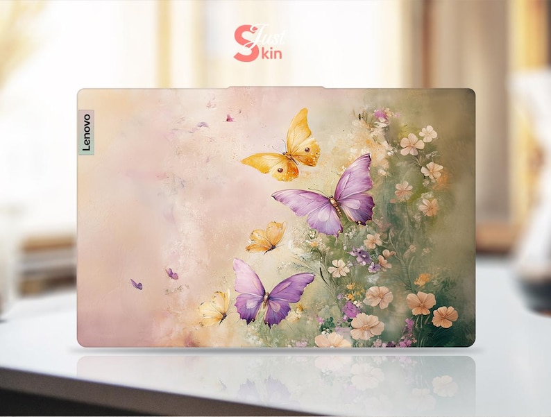 Puede incluir: Una piel para port&aacute;til rosa y blanca con un dise&ntilde;o floral con mariposas en tonos morados y amarillos. La piel tiene la palabra "Lenovo" impresa en el lado izquierdo.