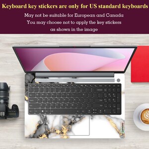 May include: A laptop computer with a white marble and gold keyboard sticker. The sticker has a black and white marble pattern with gold accents. The laptop is on a wooden surface. The text "Keyboard key stickers are only for US standard keyboards" is displayed at the top of the image. The text "May not be suitable for European and Canada" is displayed below the first line of text. The text "You may choose not to apply the key stickers as shown in the image" is displayed below the second line of text. The text "Lenovo" is displayed on the bottom right corner of the laptop.