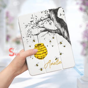 Könnte beinhalten: Weißes iPad-Case mit einer Schwarzweißzeichnung eines Astes mit einer daran hängenden Bienenwabe. Die Wabe ist gelb und mehrere Bienen fliegen um den Ast herum. Der Name Amelia ist in goldener Schrift auf dem Case geschrieben.